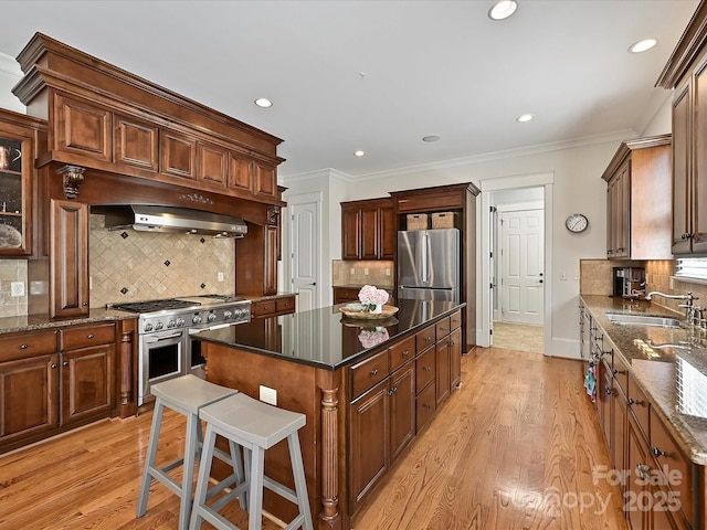 kitchen with a sink, light wood-style flooring, backsplash, a kitchen island, and appliances with stainless steel finishes