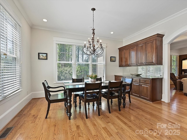 dining area with an inviting chandelier, light wood-style flooring, visible vents, arched walkways, and ornamental molding