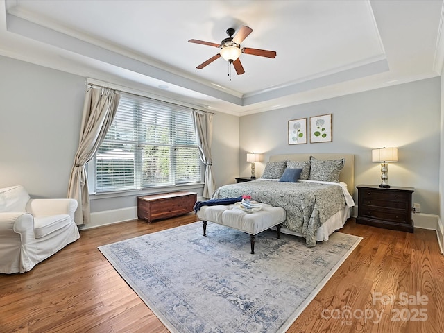 bedroom with wood finished floors, ornamental molding, ceiling fan, a tray ceiling, and baseboards