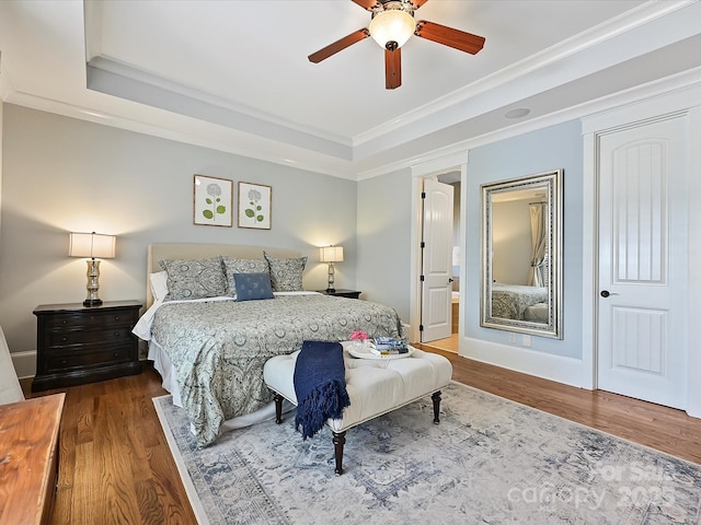 bedroom with wood finished floors, ensuite bath, crown molding, a raised ceiling, and baseboards