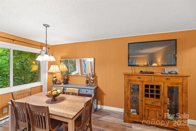 dining room with a textured ceiling, wood finished floors, baseboards, a baseboard heating unit, and a chandelier
