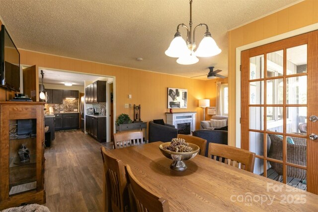 dining space featuring a textured ceiling, dark wood finished floors, ceiling fan with notable chandelier, and a fireplace