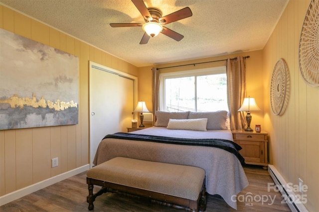 bedroom with a textured ceiling, baseboards, baseboard heating, and wood finished floors