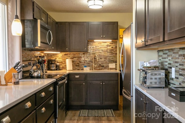 kitchen with backsplash, appliances with stainless steel finishes, dark brown cabinets, a sink, and light countertops