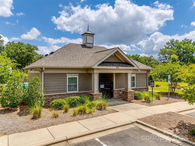 view of front of home with roof with shingles, uncovered parking, and stone siding