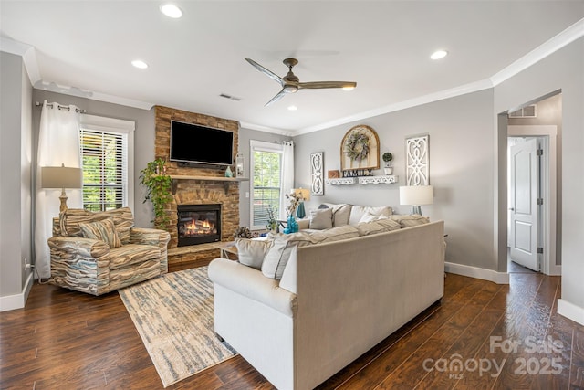 living area featuring crown molding, a fireplace, baseboards, a ceiling fan, and dark wood finished floors