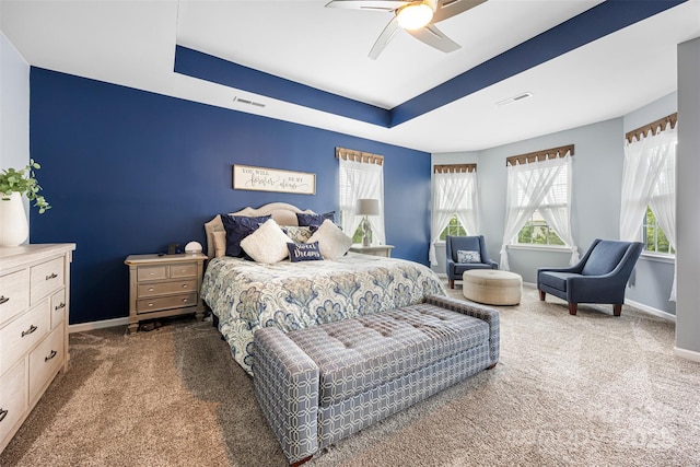 bedroom with carpet floors, a ceiling fan, baseboards, a tray ceiling, and visible vents