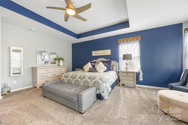 carpeted bedroom featuring a ceiling fan, a tray ceiling, visible vents, and baseboards