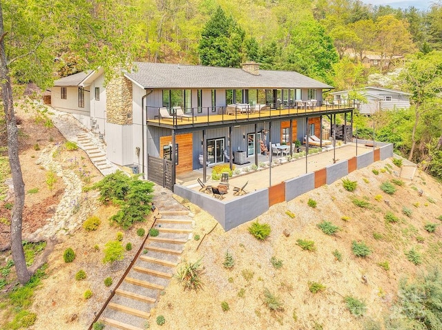 back of property featuring stairway, a deck, a chimney, and stone siding