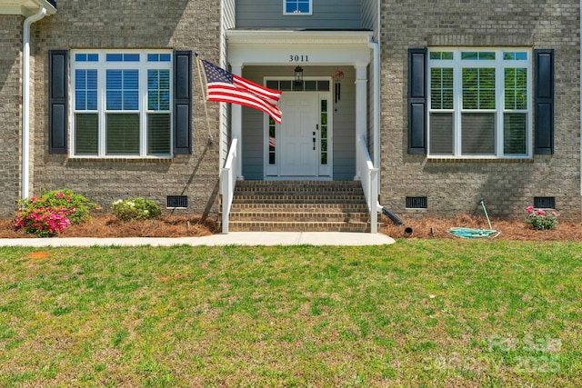 view of exterior entry featuring a yard, brick siding, and crawl space