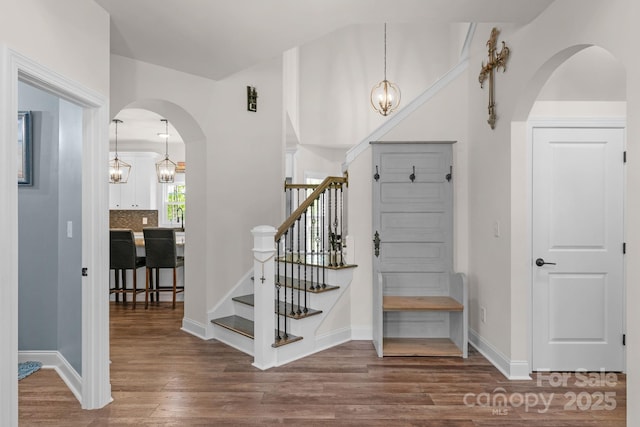 interior space featuring a notable chandelier, arched walkways, stairs, baseboards, and wood finished floors