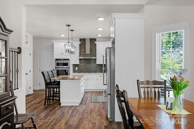 kitchen featuring a kitchen island, dark wood-style floors, wall chimney exhaust hood, white cabinetry, and appliances with stainless steel finishes