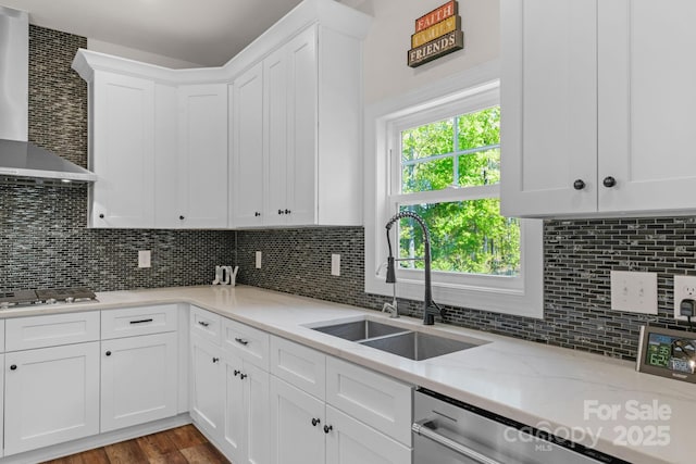 kitchen with stainless steel appliances, white cabinetry, a sink, and wall chimney exhaust hood