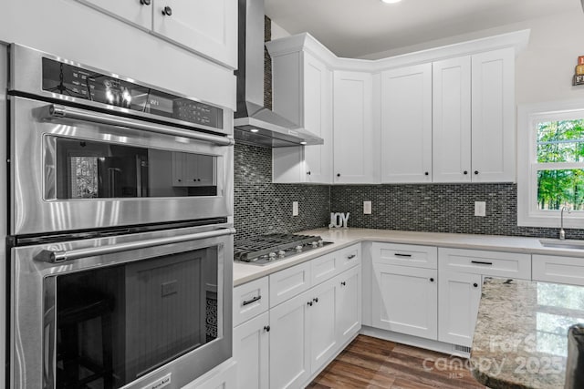 kitchen with wall chimney range hood, light countertops, stainless steel appliances, and a sink