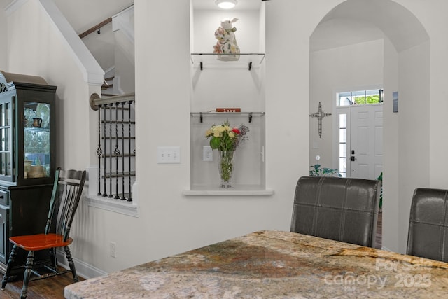 entrance foyer featuring baseboards, arched walkways, wood finished floors, and stairway