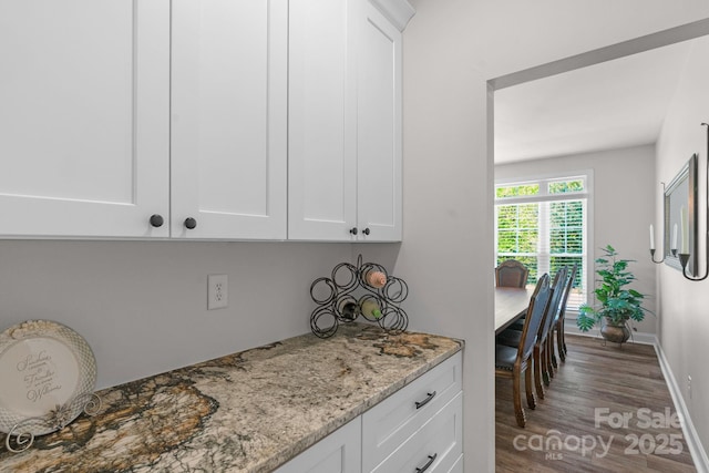 kitchen featuring baseboards, light stone countertops, wood finished floors, and white cabinetry