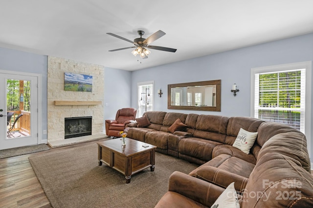 living area featuring a ceiling fan, a stone fireplace, and wood finished floors