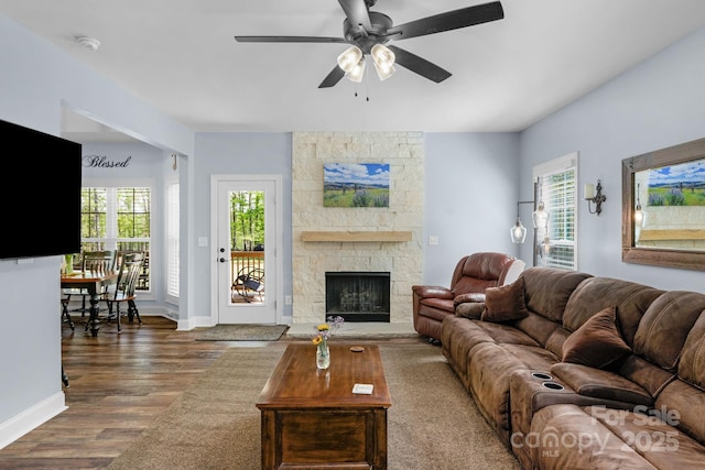 living room featuring a ceiling fan, baseboards, wood finished floors, and a fireplace