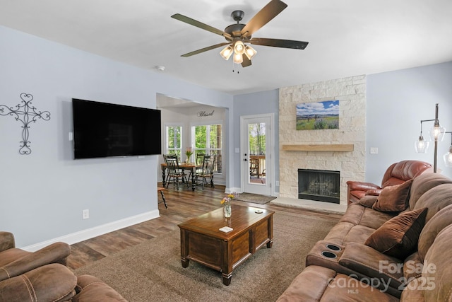 living area with a ceiling fan, baseboards, wood finished floors, and a fireplace