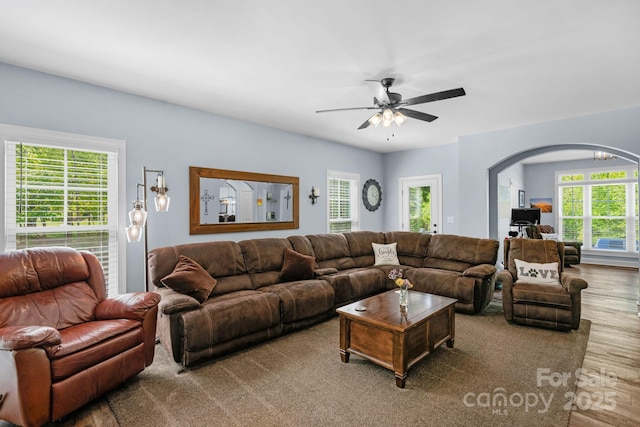 living area featuring a healthy amount of sunlight, arched walkways, a ceiling fan, and wood finished floors