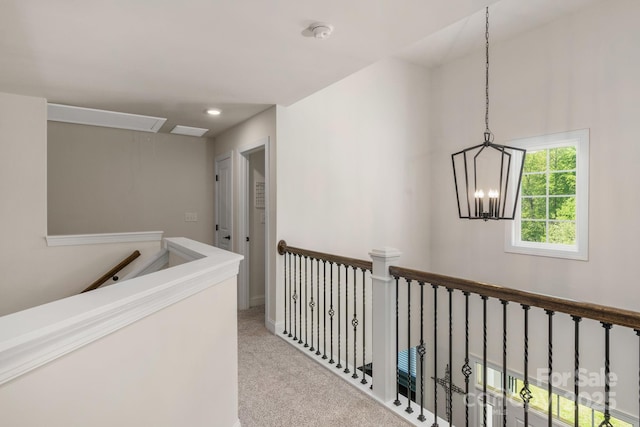 hallway with baseboards, attic access, a chandelier, carpet, and an upstairs landing