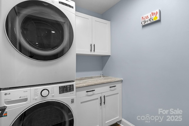 clothes washing area featuring stacked washer / drying machine and cabinet space