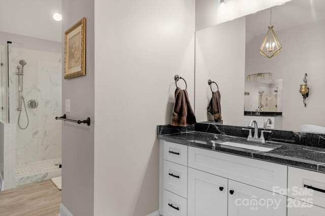 bathroom with wood finished floors, baseboards, a marble finish shower, and vanity