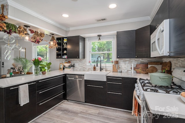 kitchen with white appliances, a sink, a peninsula, dark cabinets, and ornamental molding