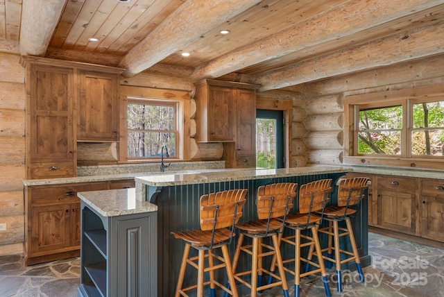 kitchen with wooden ceiling, rustic walls, brown cabinets, and plenty of natural light