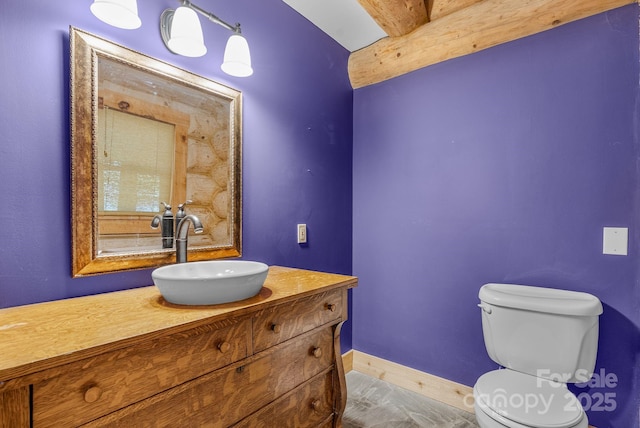 half bathroom with beam ceiling, vanity, toilet, and baseboards