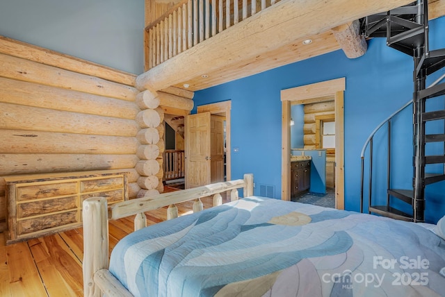 bedroom featuring rustic walls, hardwood / wood-style floors, ensuite bathroom, visible vents, and a towering ceiling