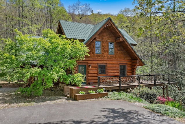 log cabin featuring a wooden deck, a forest view, metal roof, and log siding