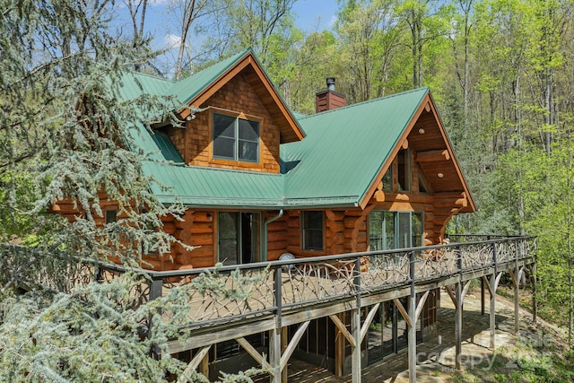 view of home's exterior with a chimney, a wooden deck, metal roof, and log siding