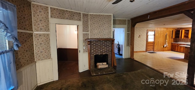 interior space with a brick fireplace, a ceiling fan, a wainscoted wall, and wallpapered walls