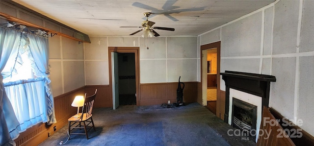 unfurnished living room featuring ceiling fan, a wainscoted wall, wooden walls, and a fireplace
