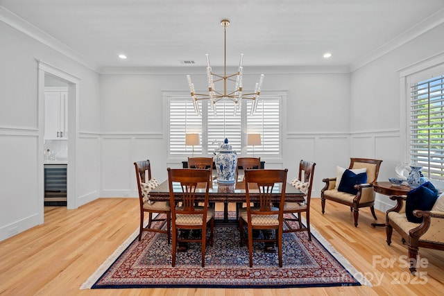 dining area featuring ornamental molding, a decorative wall, wine cooler, and a notable chandelier