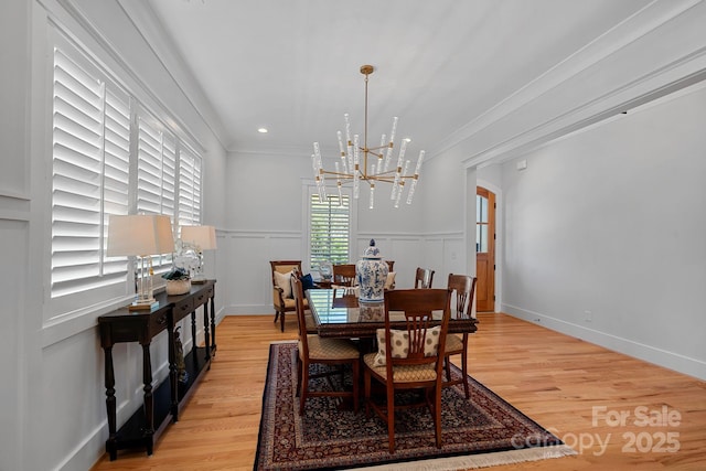 dining room with ornamental molding, a notable chandelier, light wood-style flooring, and a decorative wall
