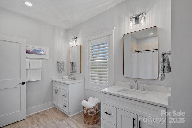 bathroom with baseboards, recessed lighting, two vanities, and a sink