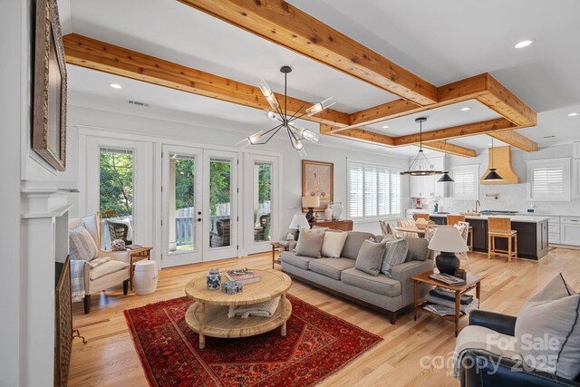 living area with an inviting chandelier, light wood-style flooring, a healthy amount of sunlight, and beam ceiling
