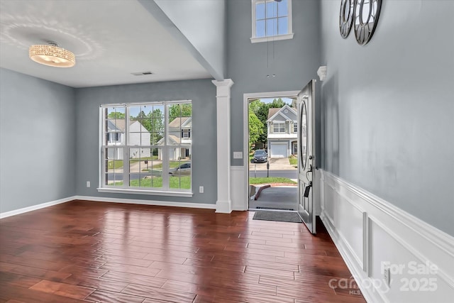 entryway with a wainscoted wall, dark wood-style flooring, ornate columns, and visible vents