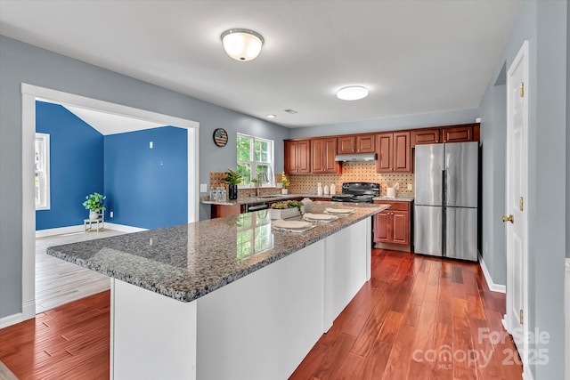 kitchen with black / electric stove, freestanding refrigerator, under cabinet range hood, and dark wood-style floors