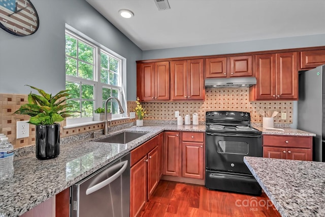 kitchen with dark wood-type flooring, under cabinet range hood, light stone counters, a sink, and appliances with stainless steel finishes