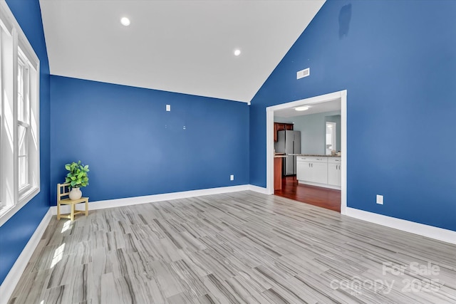unfurnished bedroom with visible vents, freestanding refrigerator, baseboards, high vaulted ceiling, and light wood-style flooring
