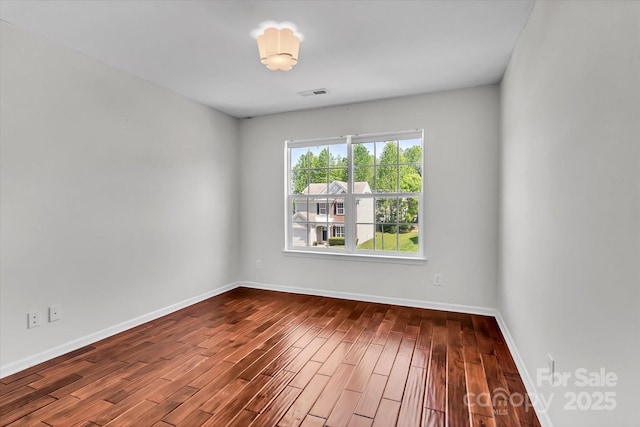 empty room with baseboards, visible vents, and dark wood-style floors
