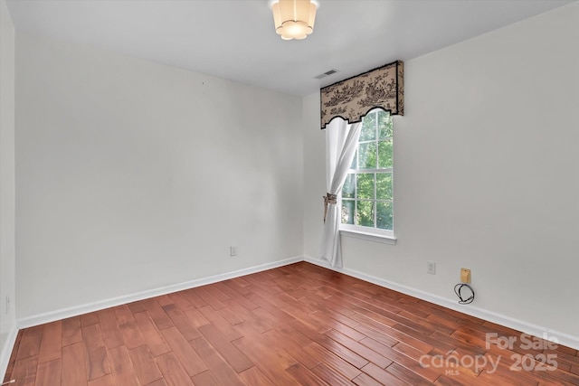 unfurnished room featuring baseboards, visible vents, and wood finished floors