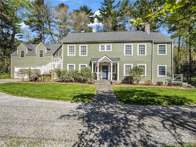 colonial-style house with a chimney, a front lawn, driveway, and a garage