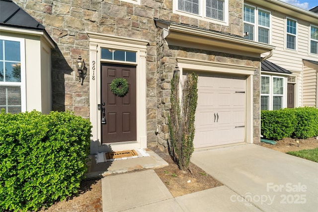 doorway to property with an attached garage, driveway, and stone siding