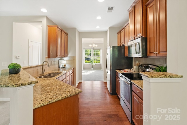 kitchen featuring stainless steel appliances, a sink, dark wood finished floors, decorative backsplash, and light stone counters