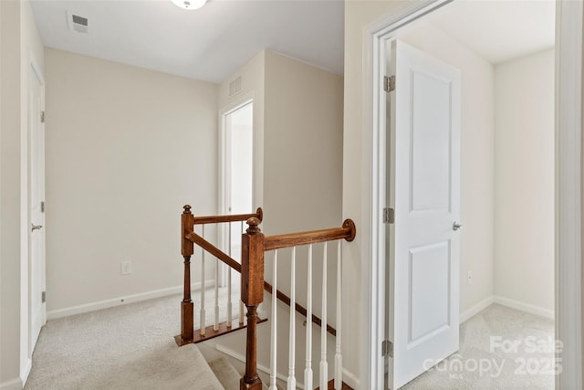 corridor with carpet floors, visible vents, and an upstairs landing