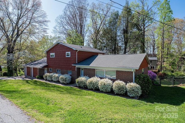view of home's exterior with a yard, a shingled roof, fence, and brick siding